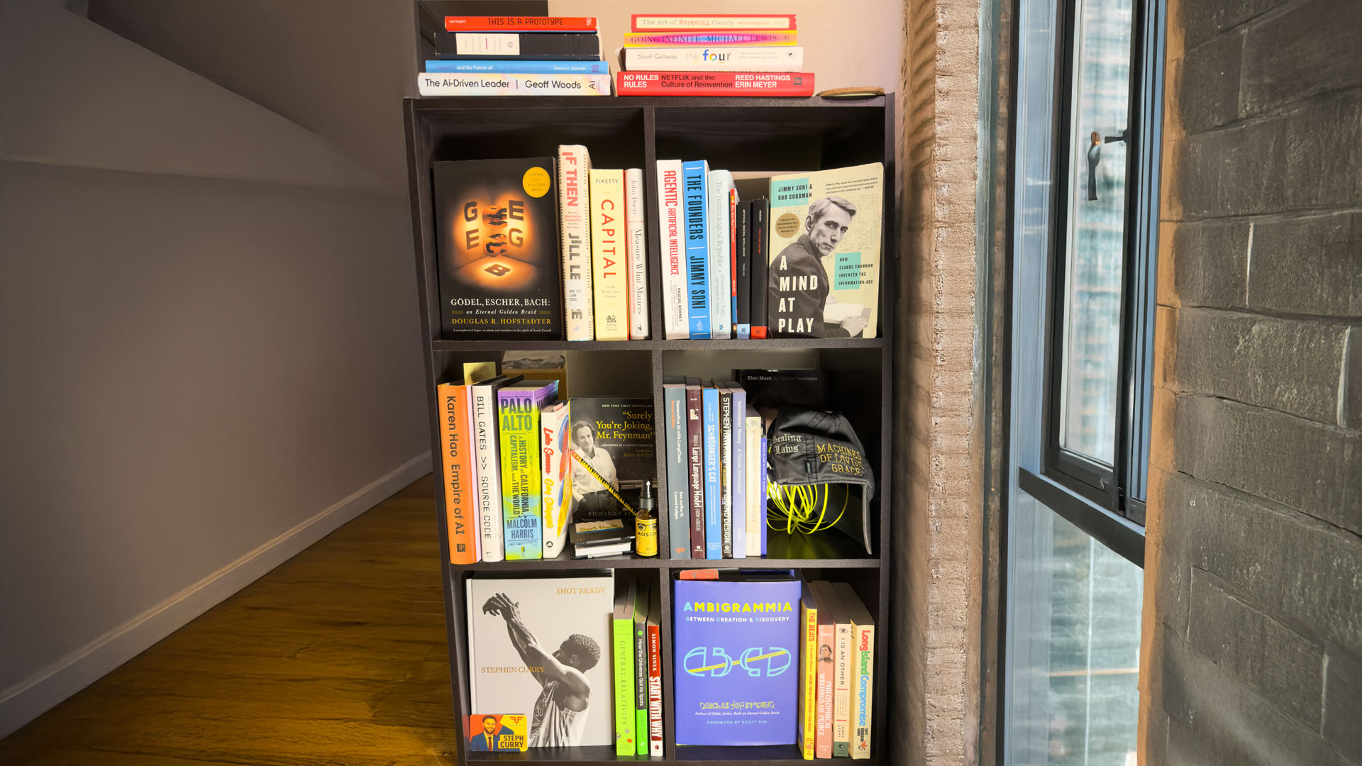 A shelf of books Bret Kerr curates as an analog RAG (retrieval-augmented generation) system: AI research, information theory, history of computing, and adjacent titles physically arranged for reference.