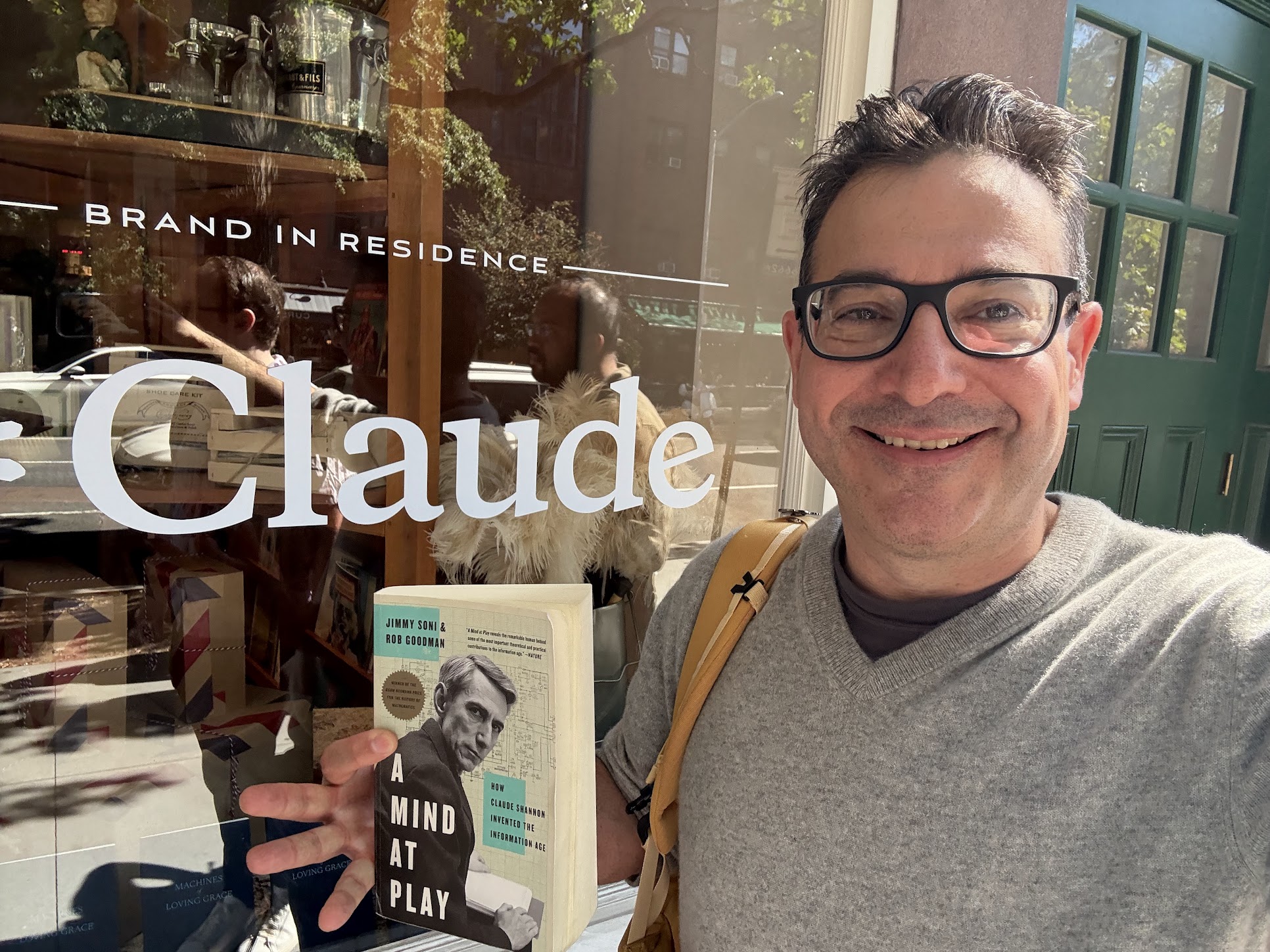 Bret Kerr at the Anthropic "Keep Thinking" brand activation in October 2025 at Graydon Carter's AirMail in New York, holding up Jimmy Soni's biography of Claude Shannon, A Mind at Play, in front of Anthropic signage celebrating the release of Claude Sonnet 4.6.
